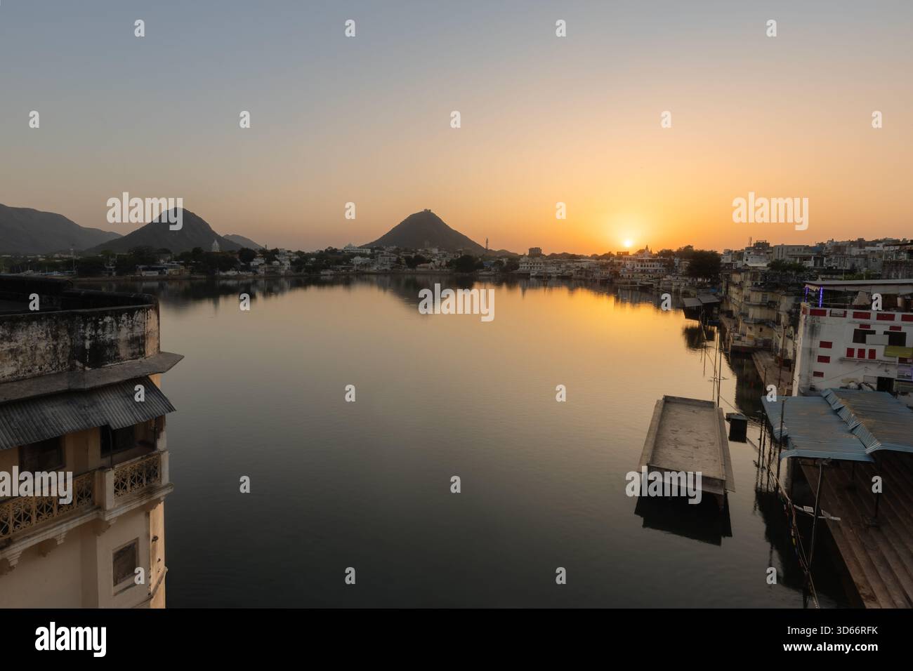 Alba sul lago Pushkar con calme acque riflettenti, ghat circostanti e colline lontane che brillano nella calda luce del mattino. Foto Stock