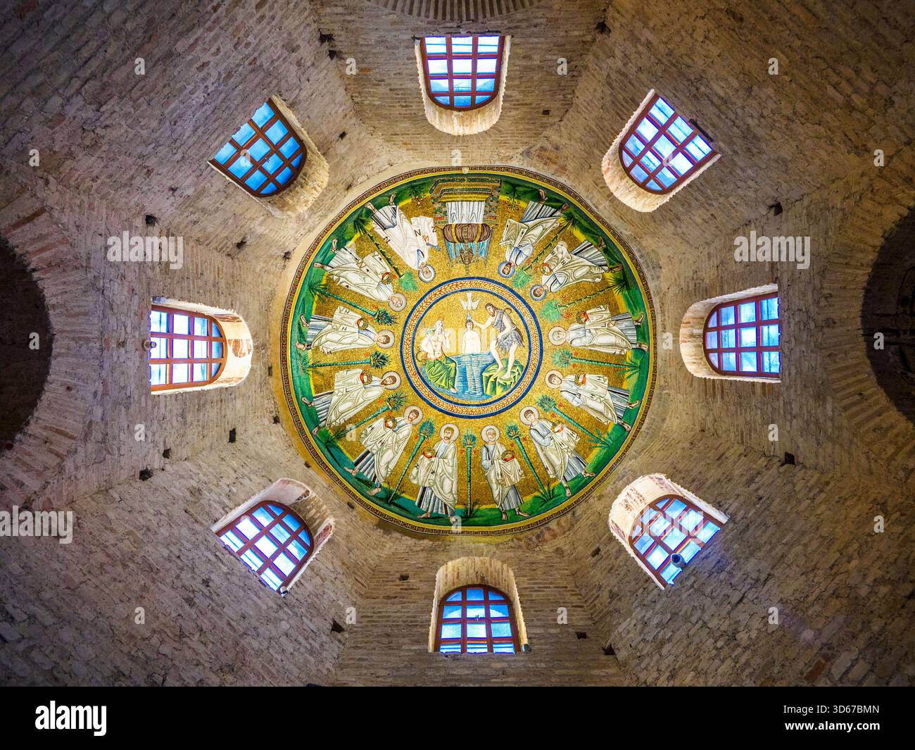 Mosaico del soffitto del Battistero Ariano. La scena del Battesimo di Cristo è circondata da una processione di Apostoli, ciascuno separato dagli altri da una palma stilizzata da cui appendono le datteri. Gli Apostoli hanno una corona gioiellata nelle loro mani velate, tranne San Pietro, che ha una grande chiave, e San Paolo, che tiene un rotolo e una rappresentazione del fuso che usa nel suo lavoro sul velo. Il Battistero ariano è un edificio battesimale cristiano eretto dal re ostrogoto Teodorico il grande tra la fine del V secolo e l'inizio del vi secolo d.C. - Ravenna Italia Foto Stock