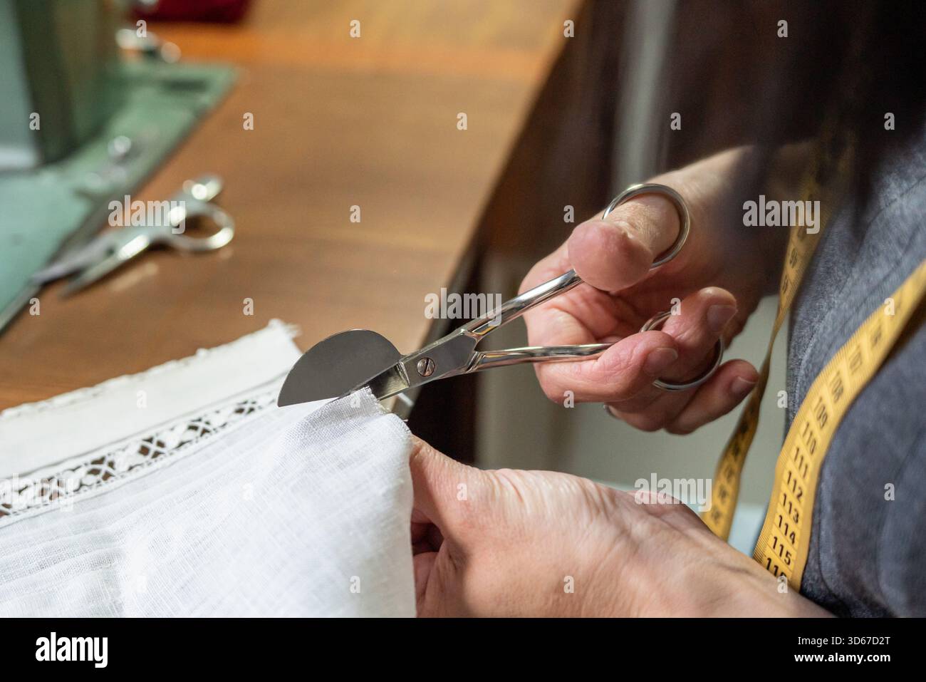 Taglio manuale di tessuto bianco con finiture in pizzo utilizzando forbici sartoriali curve Foto Stock