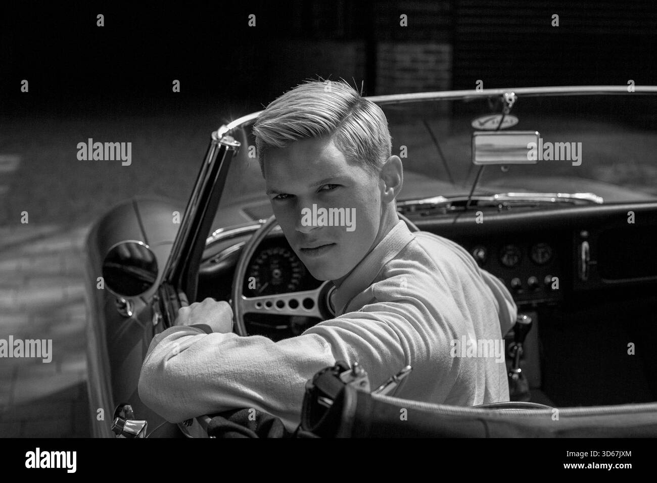 Un giovane seduto al posto di guida di una classica Jaguar e-Type serie 1 Roadster 1964, che guarda direttamente la telecamera. Foto Stock