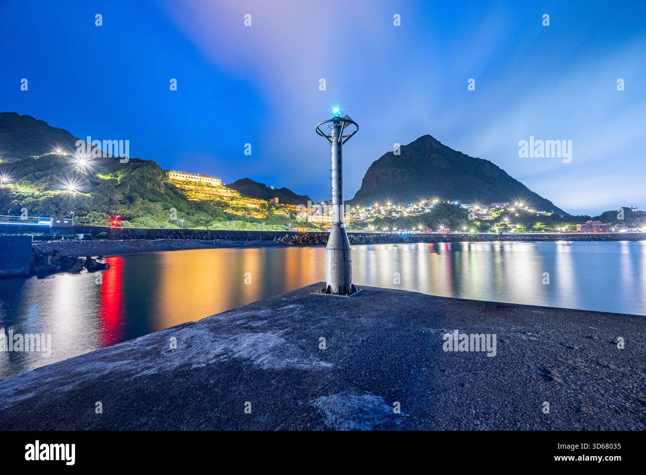 Taiwan Northeast Habor.Un molo solitario si estende fino all'abbraccio della notte, dove le luci della città brillano e le montagne tacciono sotto un cielo stellato. Foto Stock