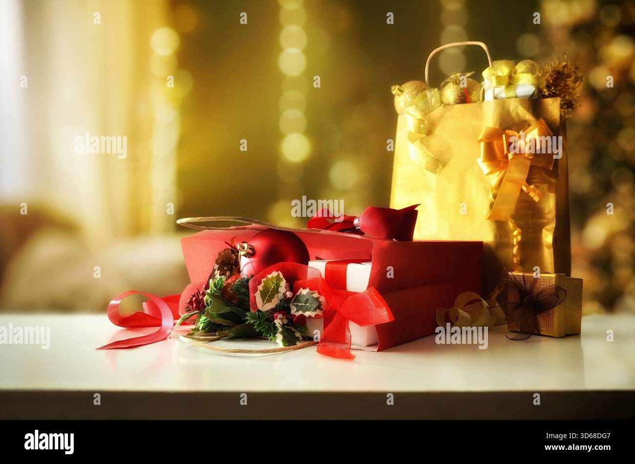 Borse regalo e decorazioni complete rosse e dorate sul tavolo in un caldo soggiorno con albero di Natale e sfondo luci. Foto Stock