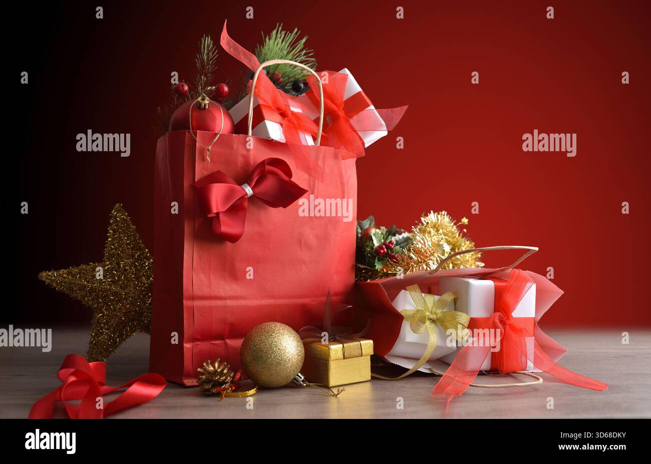 Concetto di fare regali a Natale con sacchetti regalo rossi pieni di pacchetti regalo e decorazioni natalizie su un tavolo in legno e sfondo rosso sfumato. Foto Stock