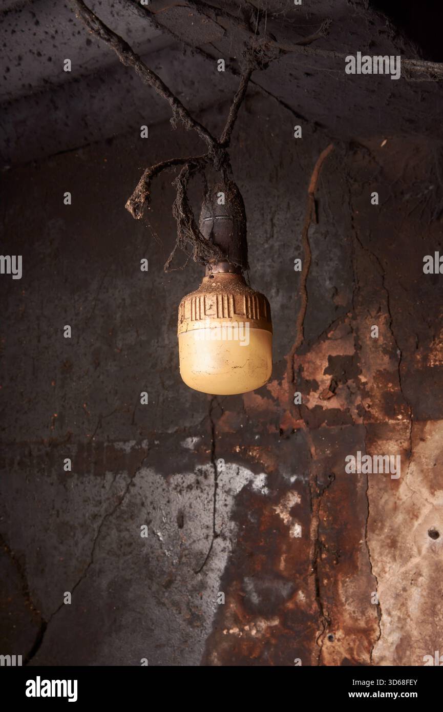 primo piano di lampade sporche, diffusore in plastica giallo incastrato nella sporcizia e fuliggine appesa al soffitto scuro, concetto di negligenza e decadimento industriale Foto Stock