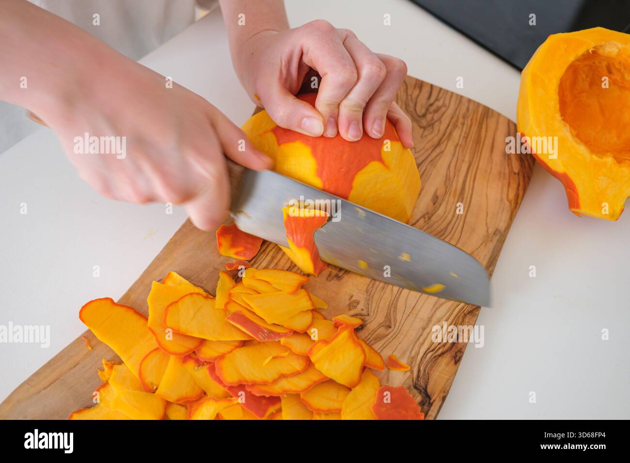 Una persona sbuccia con cura una zucca su un tagliere di legno Foto Stock