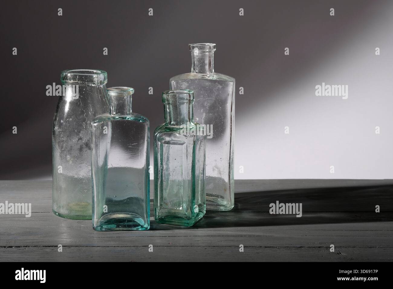 quattro vecchie bottiglie di vetro su un piano da tavolo dipinto di grigio Foto Stock