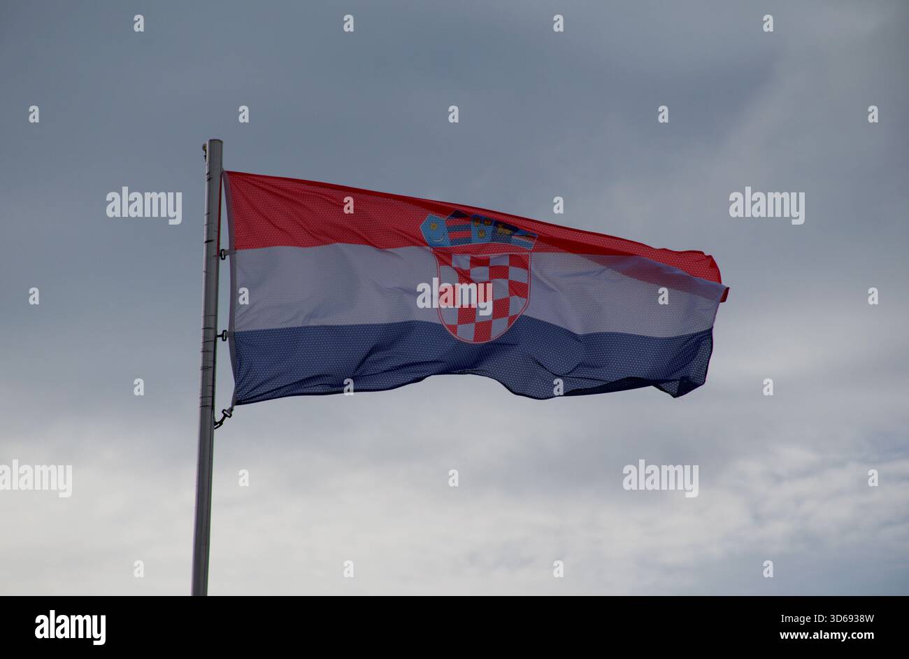 Vibrante bandiera croata con stemma che ondeggia in forte vento sotto un cielo nuvoloso. Patriottismo, identità nazionale, Europa, viaggi. Foto Stock