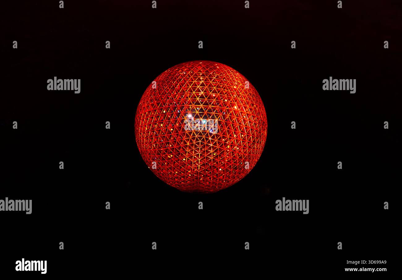Una sfera rossa radiosa composta da reticoli triangolari si illumina in modo vivace su uno sfondo nero, mostrando una complessa simmetria geometrica Foto Stock