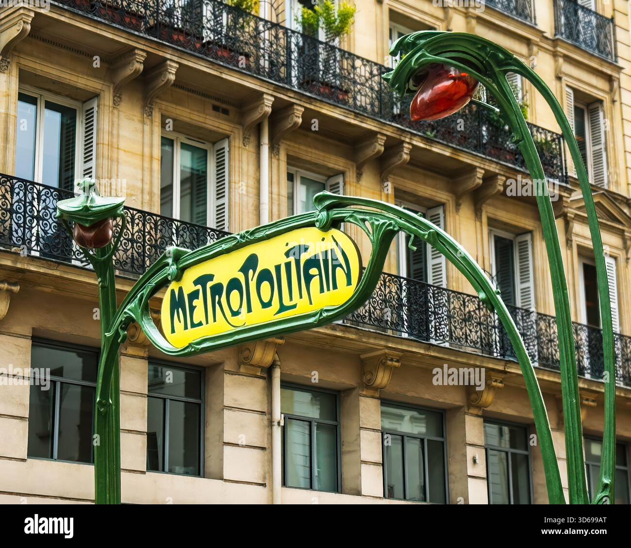 Un elegante cartello della metropolitana art nouveau sorge di fronte ad un tradizionale edificio parigino. Il metallo verde curvo e i colori vivaci aggiungono fascino. Foto Stock