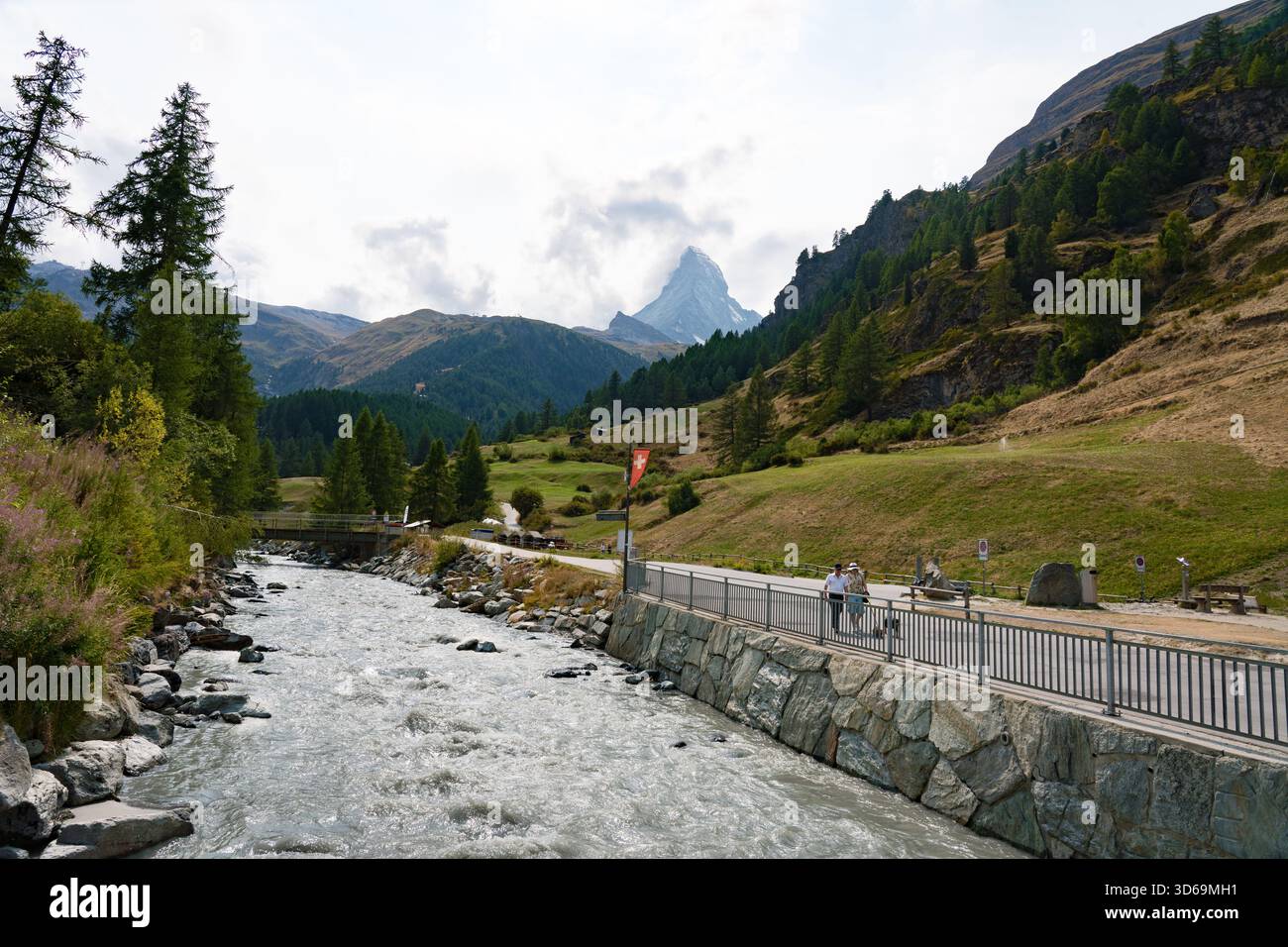 Vallese, Svizzera - 19 agosto 2025: Vista del Cervino con un fiume che scorre attraverso un canale, sentiero escursionistico e verdi pascoli delle Alpi svizzere. Foto Stock