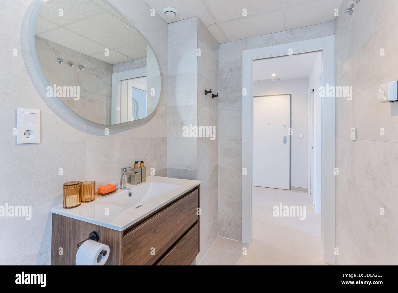 Bagno contemporaneo con lavandino in legno, specchio ovale, illuminazione soffusa e pareti in piastrelle minimaliste Foto Stock