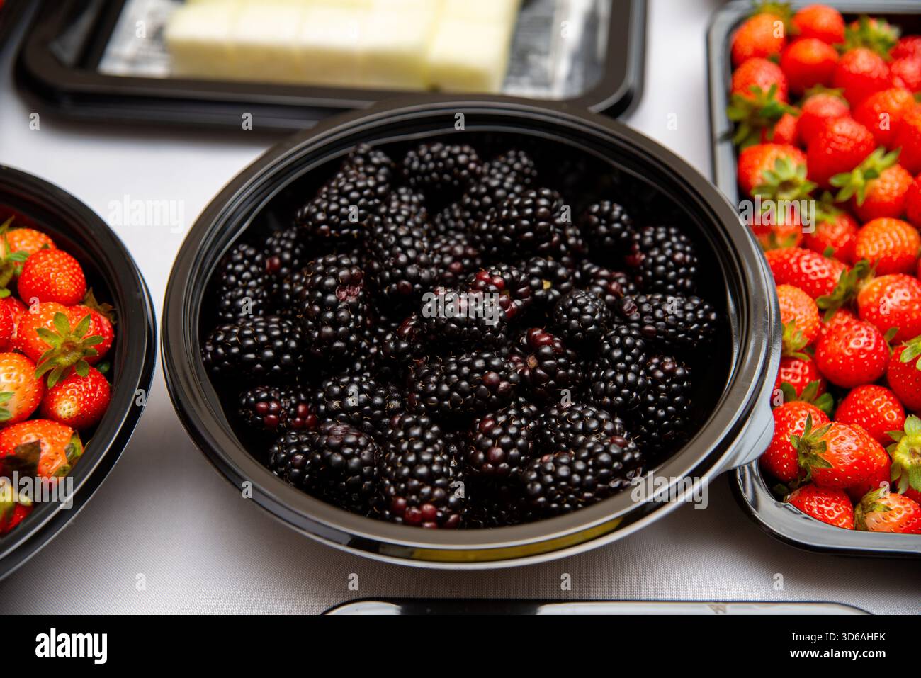 Una selezione di bacche fresche, tra cui more e fragole, visualizzate in una ciotola nera. ideale per temi alimentari e di stile di vita sano, con vi Foto Stock