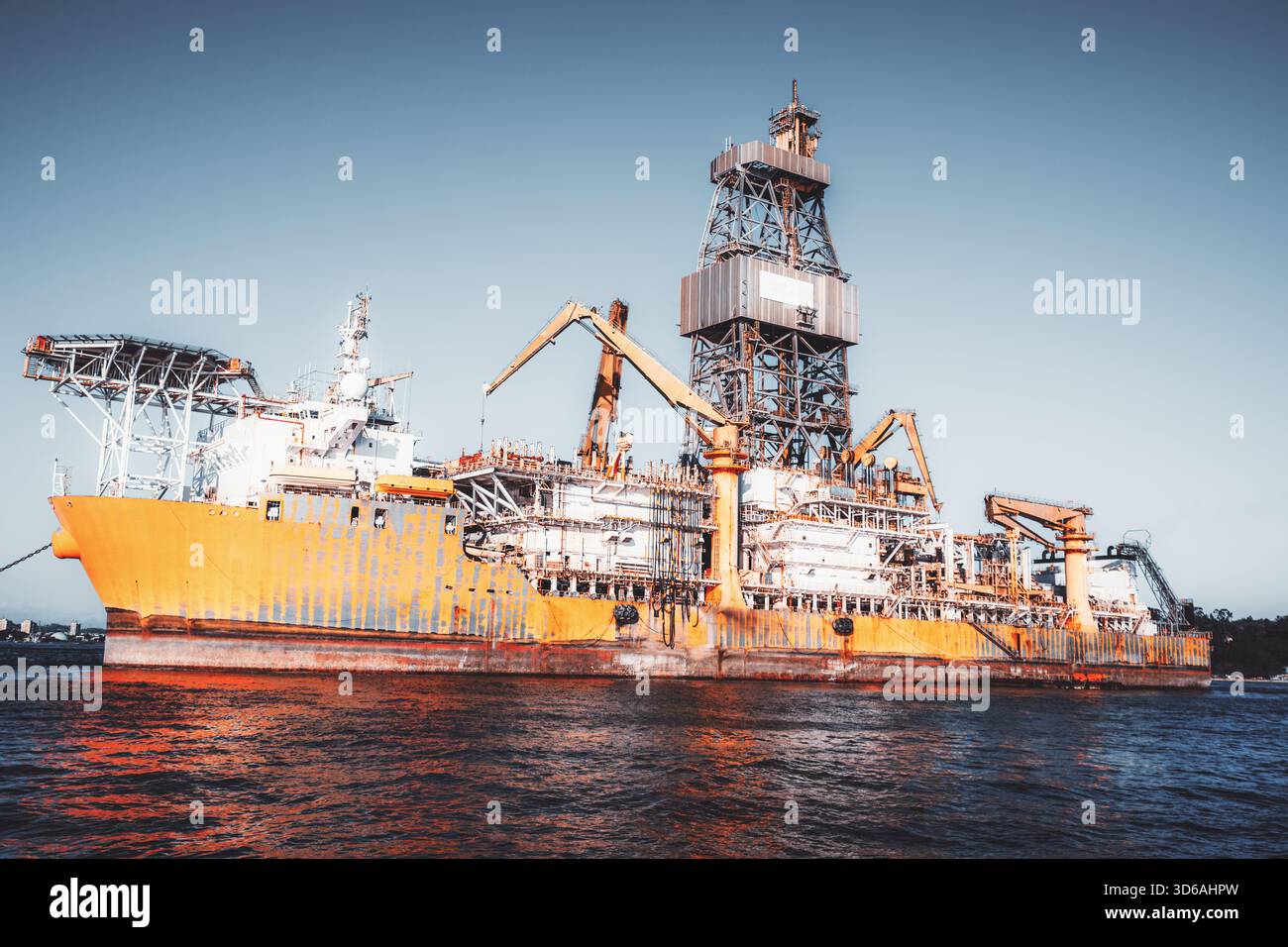 Enorme imbarcazione industriale offshore con imponente struttura di perforazione, gru pesanti e complessi telai metallici illuminati da una luce calda sopra la ripplin Foto Stock