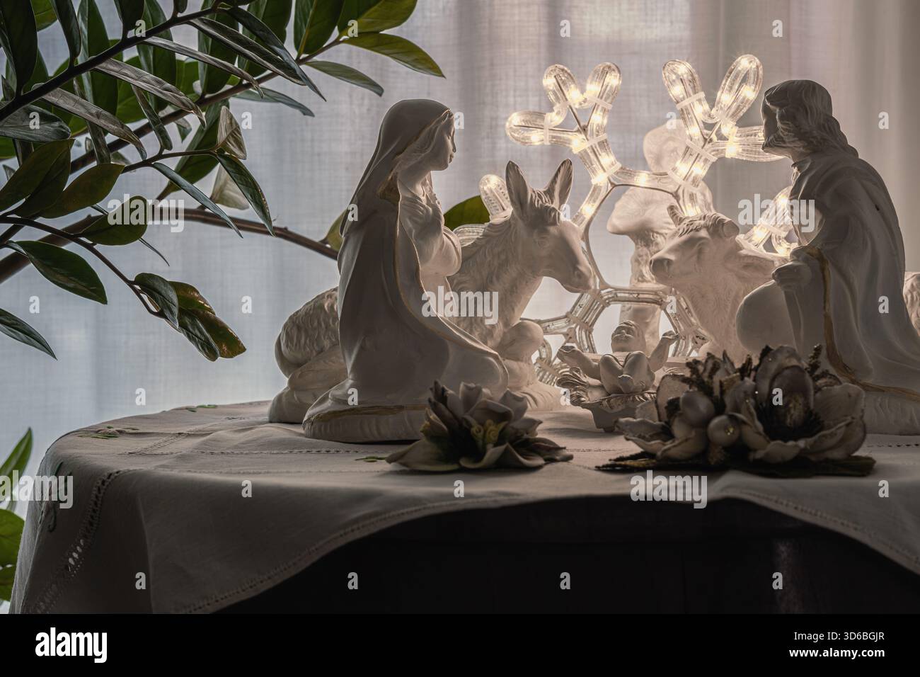 Statuette di presepi in ceramica raffiguranti Maria, Giuseppe e il bambino Gesù con un asino e un bestiame su un panno ricamato, accanto a un fiocco di neve illuminato Foto Stock
