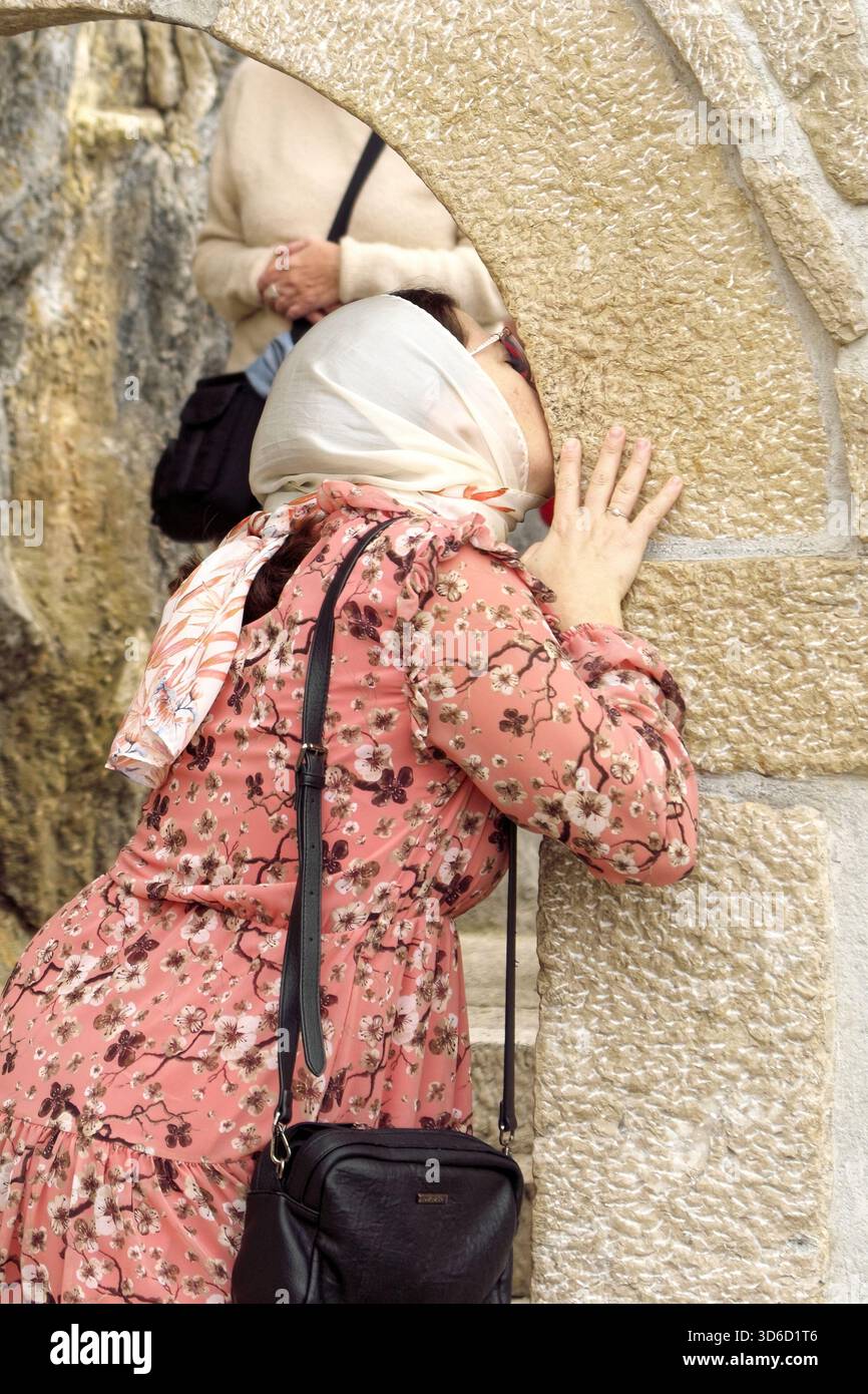 Un pellegrino sta baciando il muro di pietra all'ingresso della chiesa di roccia di Ostrog come segno di devozione, Danilovgrad, Montenegro (donna) Foto Stock