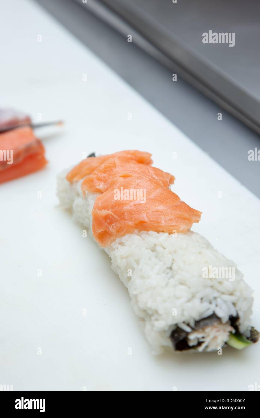 Una vista del processo di preparazione di un sushi roll in una stazione di ingredienti di un ristorante. Foto Stock