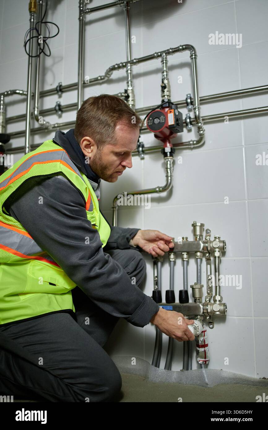 Uomo caucasico di mezza età che ispeziona il sistema idraulico industriale in ambienti chiusi Foto Stock