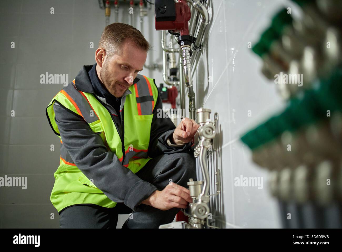 Uomo caucasico di mezza età che regola i tubi industriali nella sala utilità Foto Stock