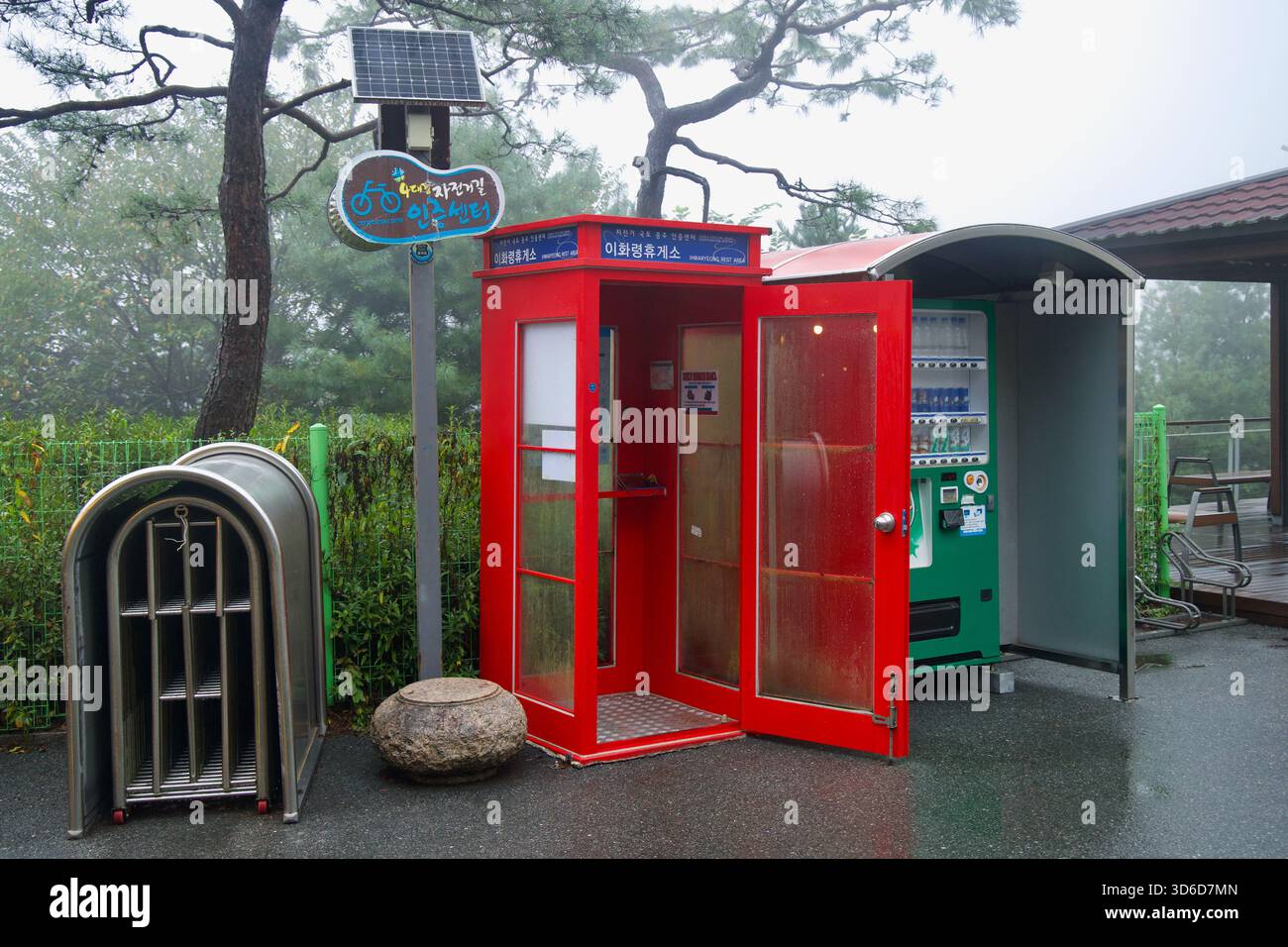 Un chiosco rosso ospita il francobollo presso il centro di certificazione di Ihwaryeong accanto a un distributore automatico all'aperto e a un portabiciclette mentre la nebbia ricopre l'Ihwa Pass Overloo Foto Stock