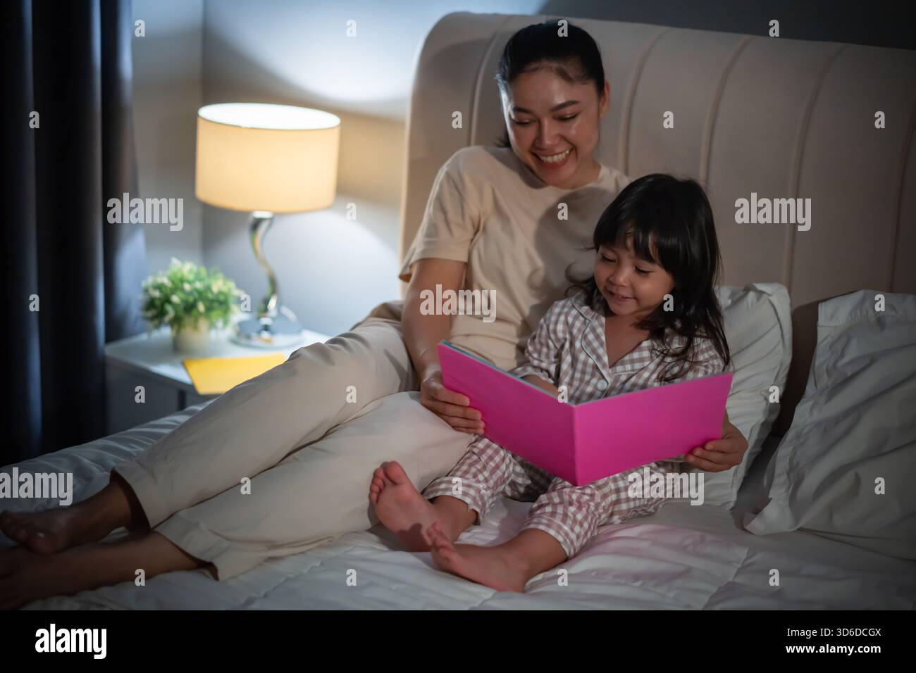 la madre ha letto la storia nel libro per la bambina su un letto di notte Foto Stock