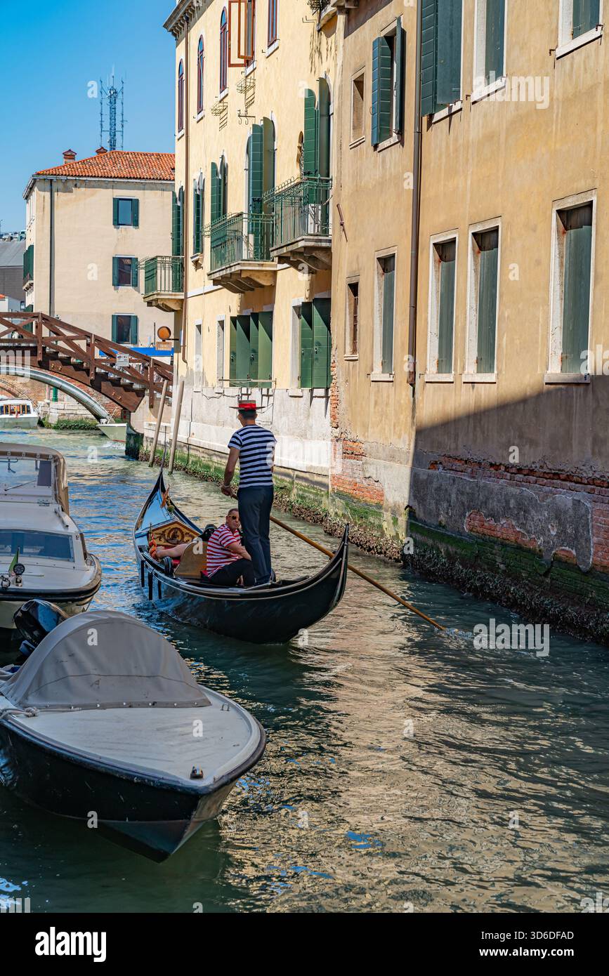 Vista romantica di un canale veneziano con una gondola che scivola tra edifici storici, riflessi d'acqua calmi che creano un'atmosfera senza tempo Foto Stock