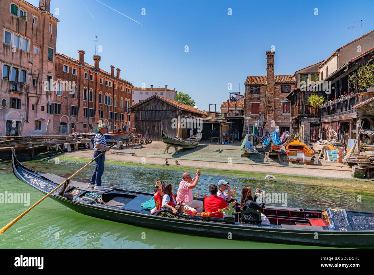 Romantico canale veneziano con una gondola e un gondoliere che scorrono davanti a un laboratorio di gondola, edifici storici e riflessi d'acqua calme che creano un'atmosfera senza tempo Foto Stock