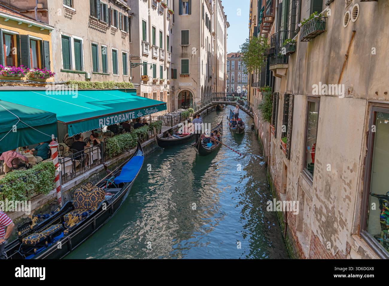 Vista romantica di un canale veneziano con una gondola e un gondoliere che scivolano attraverso acque calme, edifici storici e riflessi che creano un fascino senza tempo. Foto Stock