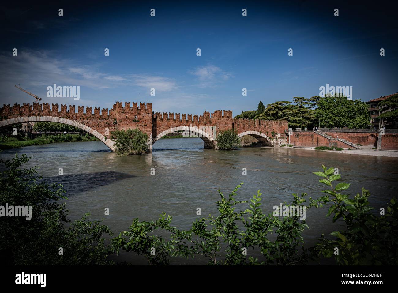 Vista panoramica di uno storico ponte in pietra a Verona, Italia, con il fiume che scorre sotto e la classica architettura italiana che circonda la scena. Foto Stock