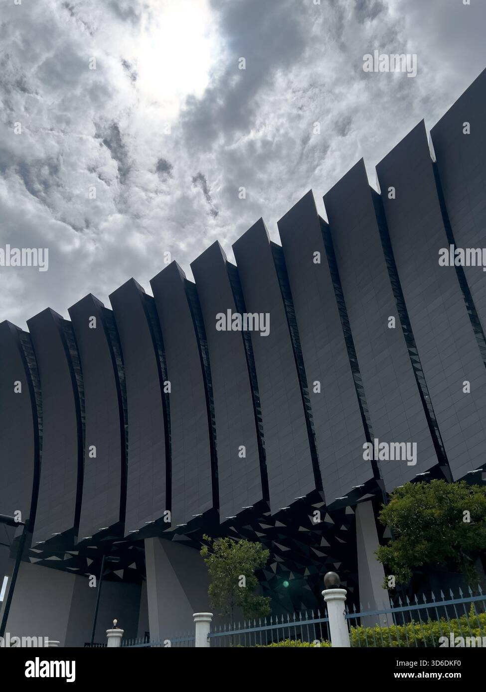 Una grande facciata di un edificio contemporaneo dal design ondulato o a costine, vista drammaticamente contro un cielo coperto. Foto Stock