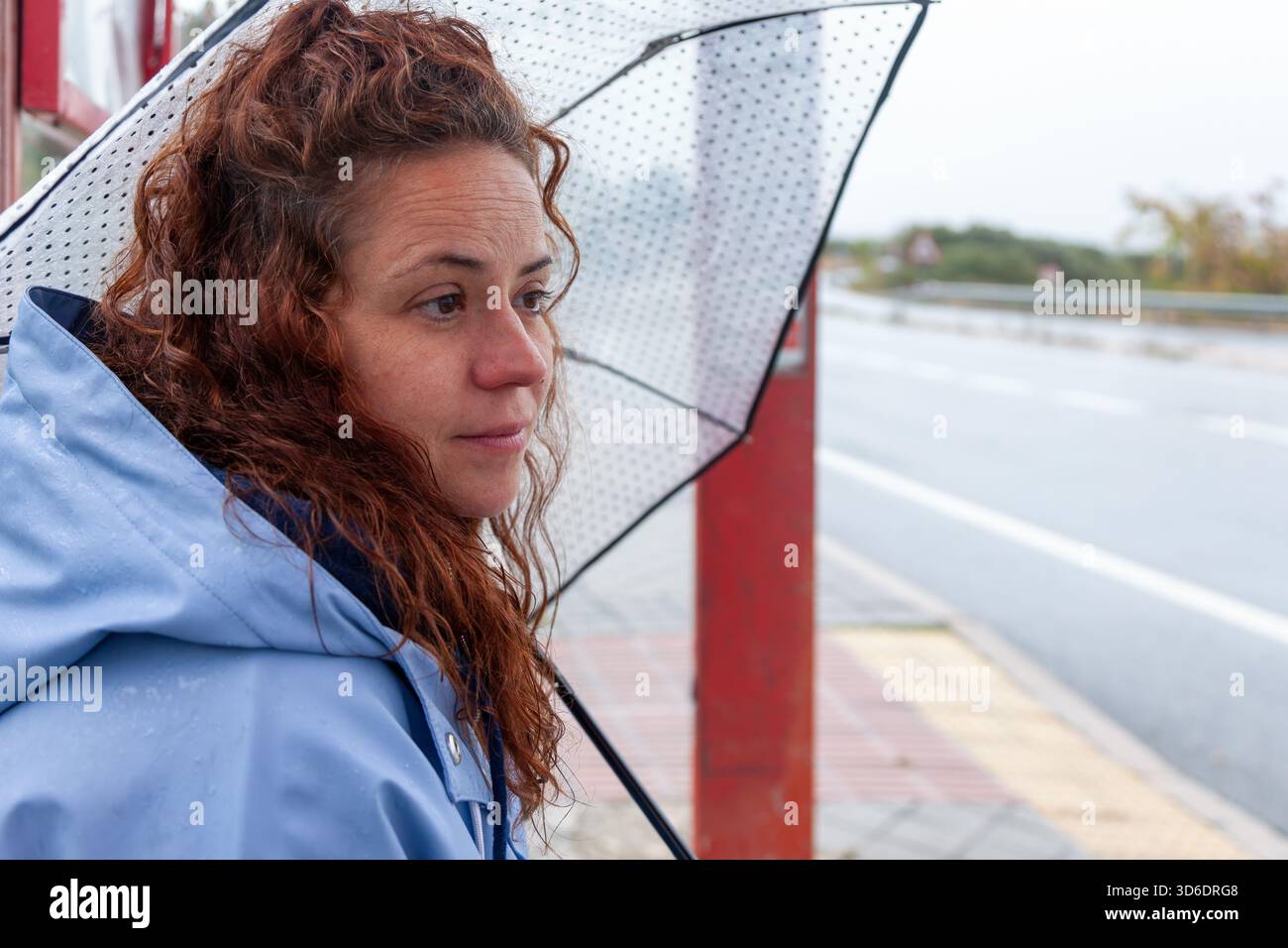 Uthentic Lifestyle: Donna con ombrello alla fermata dell'autobus in tempo piovoso Foto Stock