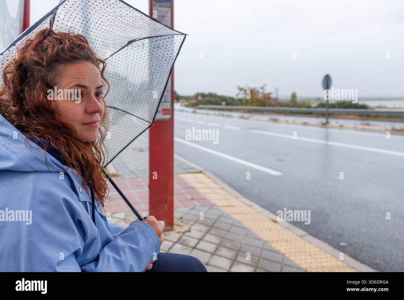 Vera giovane donna in Blue Raincoat in attesa dell'autobus in un giorno di pioggia Foto Stock