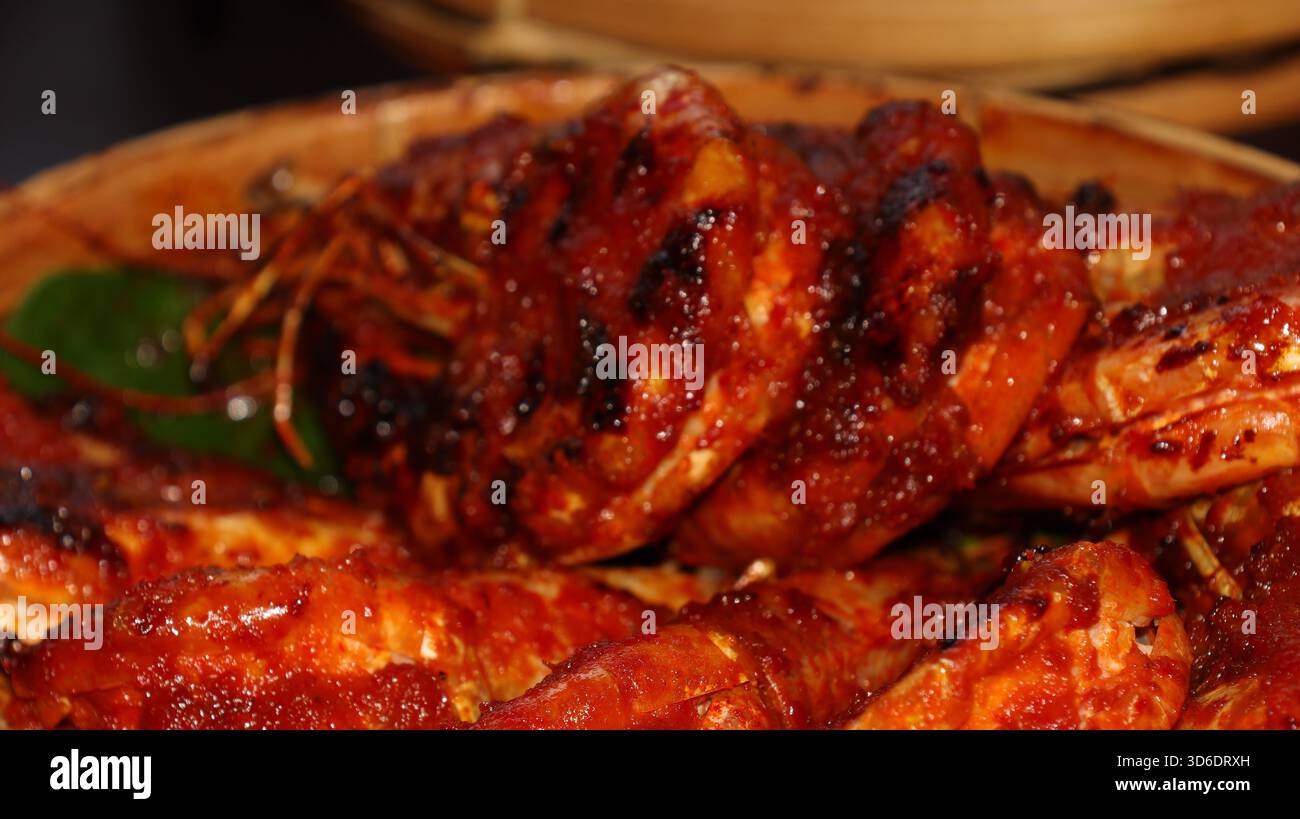 Gamberi grigliati speziati indonesiani ricoperti di salsa al peperoncino rosso, serviti su foglie di banana nel cestino di bambù. Autentica cucina asiatica a base di pesce, tradizionale Foto Stock