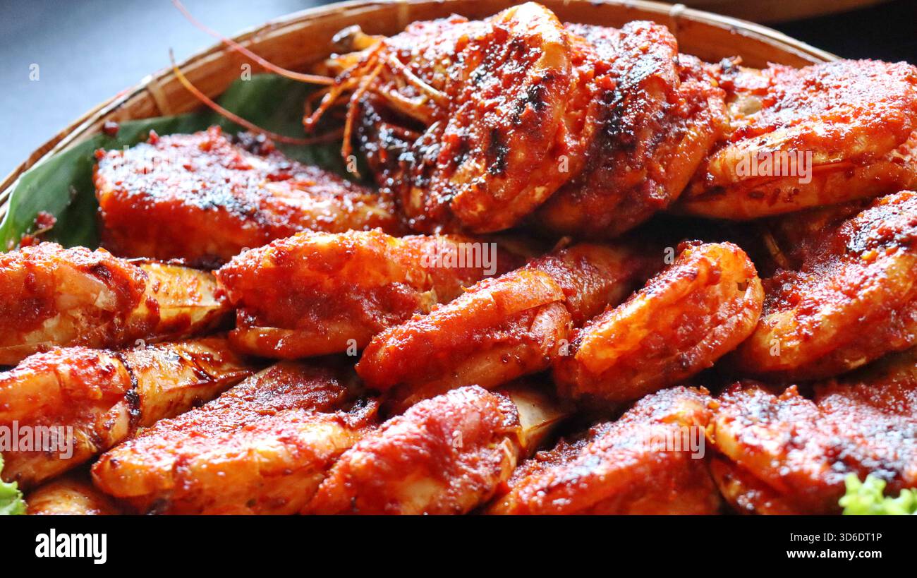 Gamberi grigliati speziati indonesiani ricoperti di salsa al peperoncino rosso, serviti su foglie di banana nel cestino di bambù. Autentica cucina asiatica a base di pesce, tradizionale Foto Stock