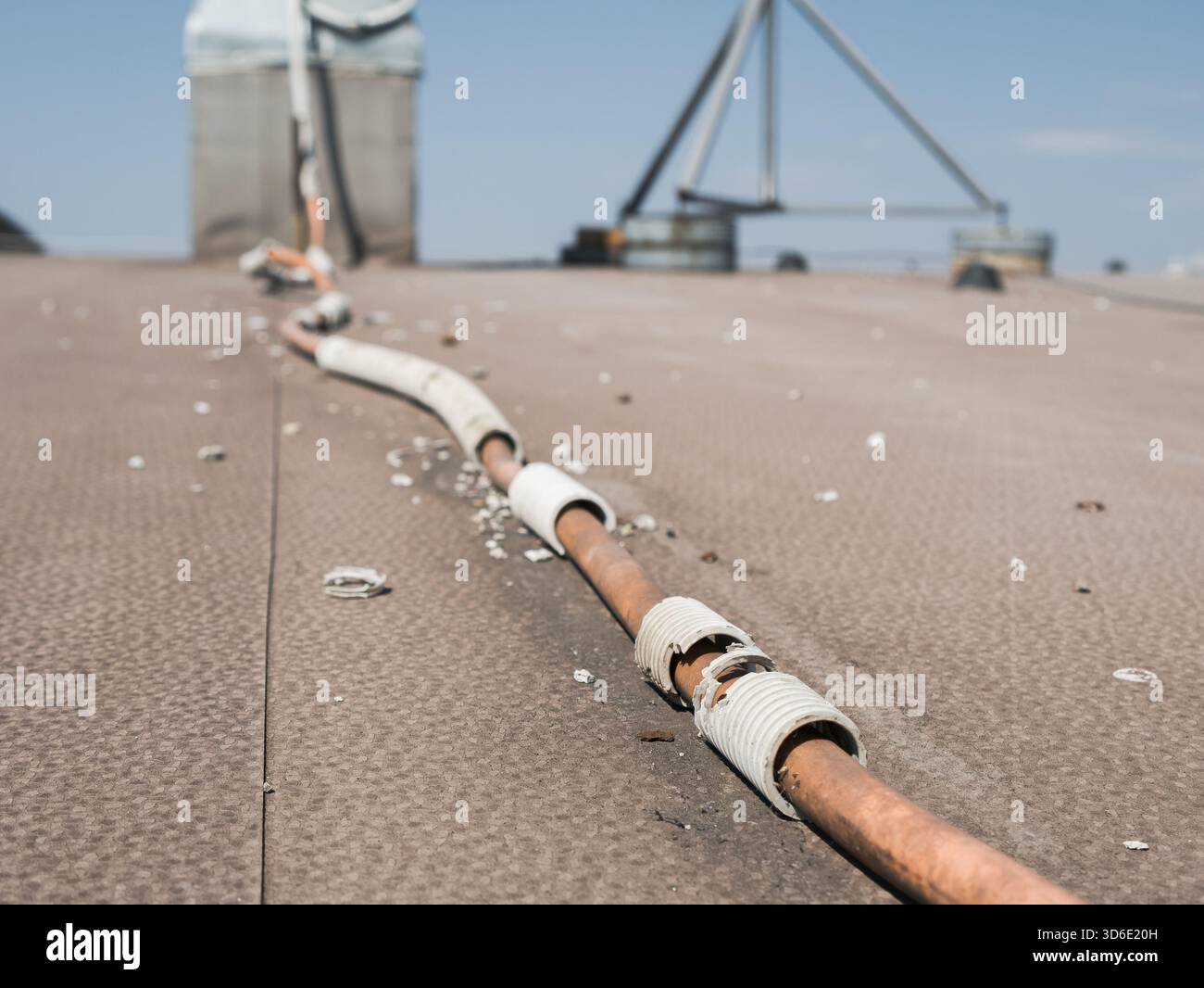 Un condotto in plastica ondulata flessibile rotto che espone i cavi elettrici sul tetto di un edificio, sottolineando i rischi di sicurezza elettrica e di alimentazione Foto Stock