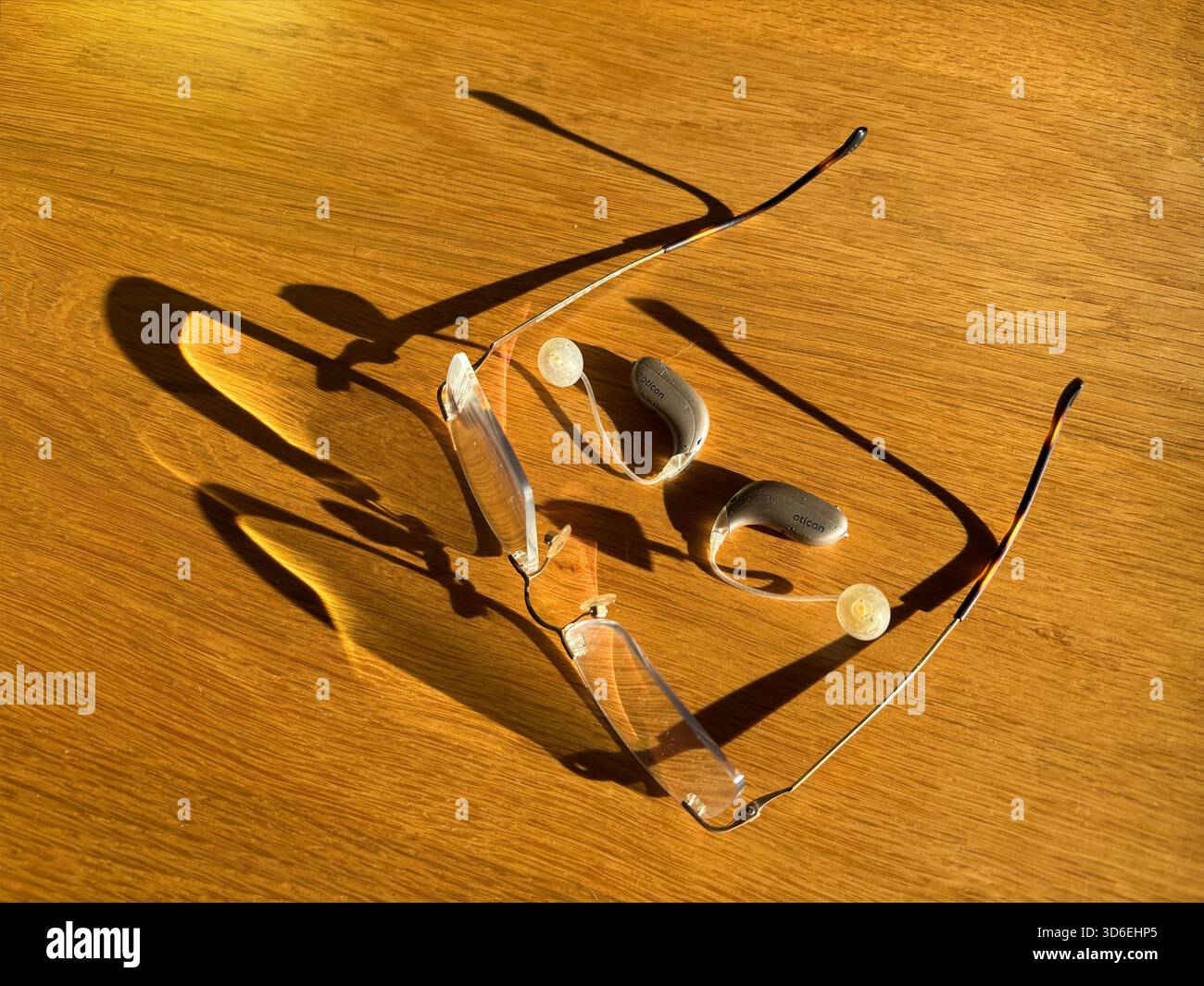 Occhiali e apparecchi acustici su un tavolo in legno sotto la luce del sole. - Immagine stock catturata con smartphone