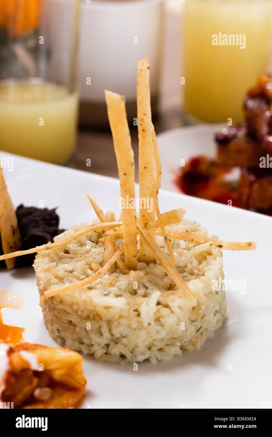 Un attraente piatto di riso messicano guarnito con croccanti strisce di tortilla, servito con una varietà di altri elementi della cucina messicana, tra cui la salsa Foto Stock