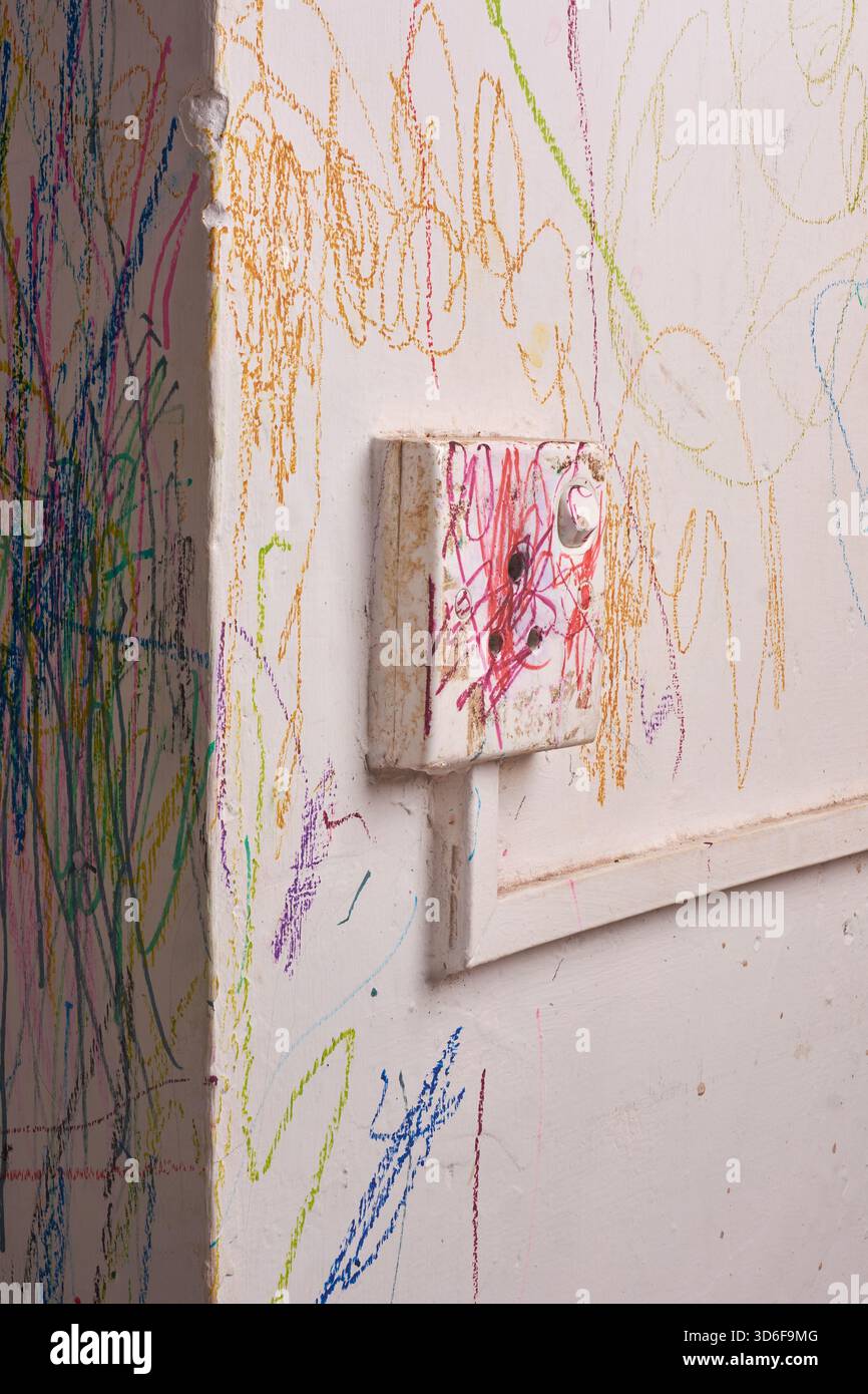 primo piano di pareti bianche ricoperte da scarabocchi colorati per bambini e scatola di commutazione usurata con segni di pastello rossi, disegni astratti e disordinati sulla superficie in gesso Foto Stock