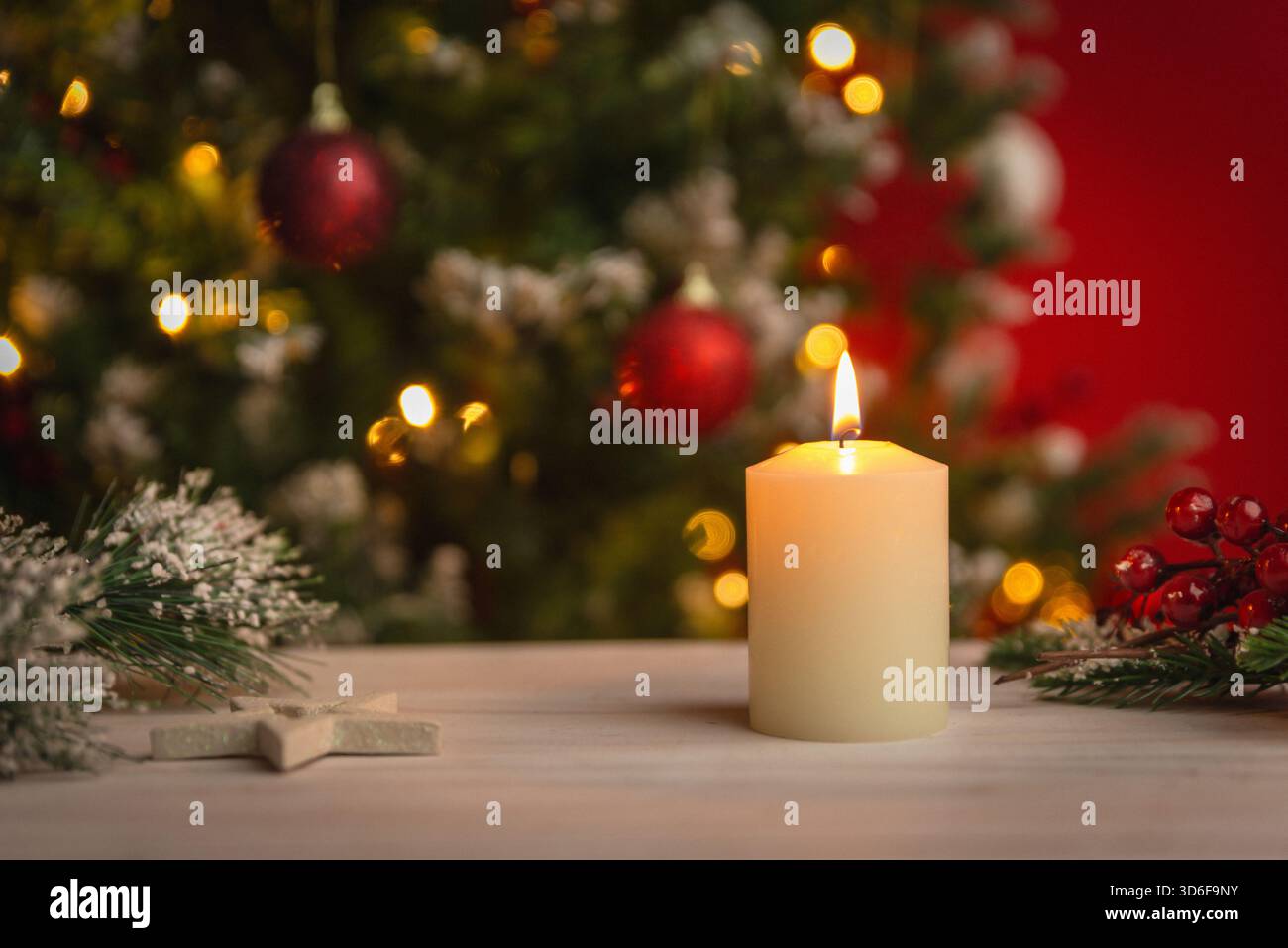 Calda candela di Natale illuminata su un tavolo in legno con luci festive e ornamenti delicatamente sfocati sullo sfondo per temi stagionali Foto Stock