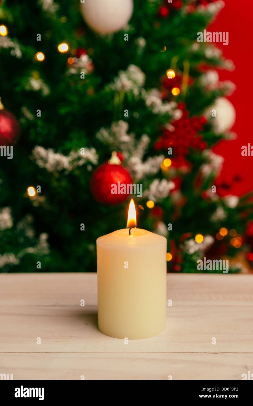 Candela di Natale verticale che si illumina dolcemente con decorazioni sfocate sugli alberi natalizi sullo sfondo, ideale per le cartoline stagionali e per le calde immagini natalizie Foto Stock