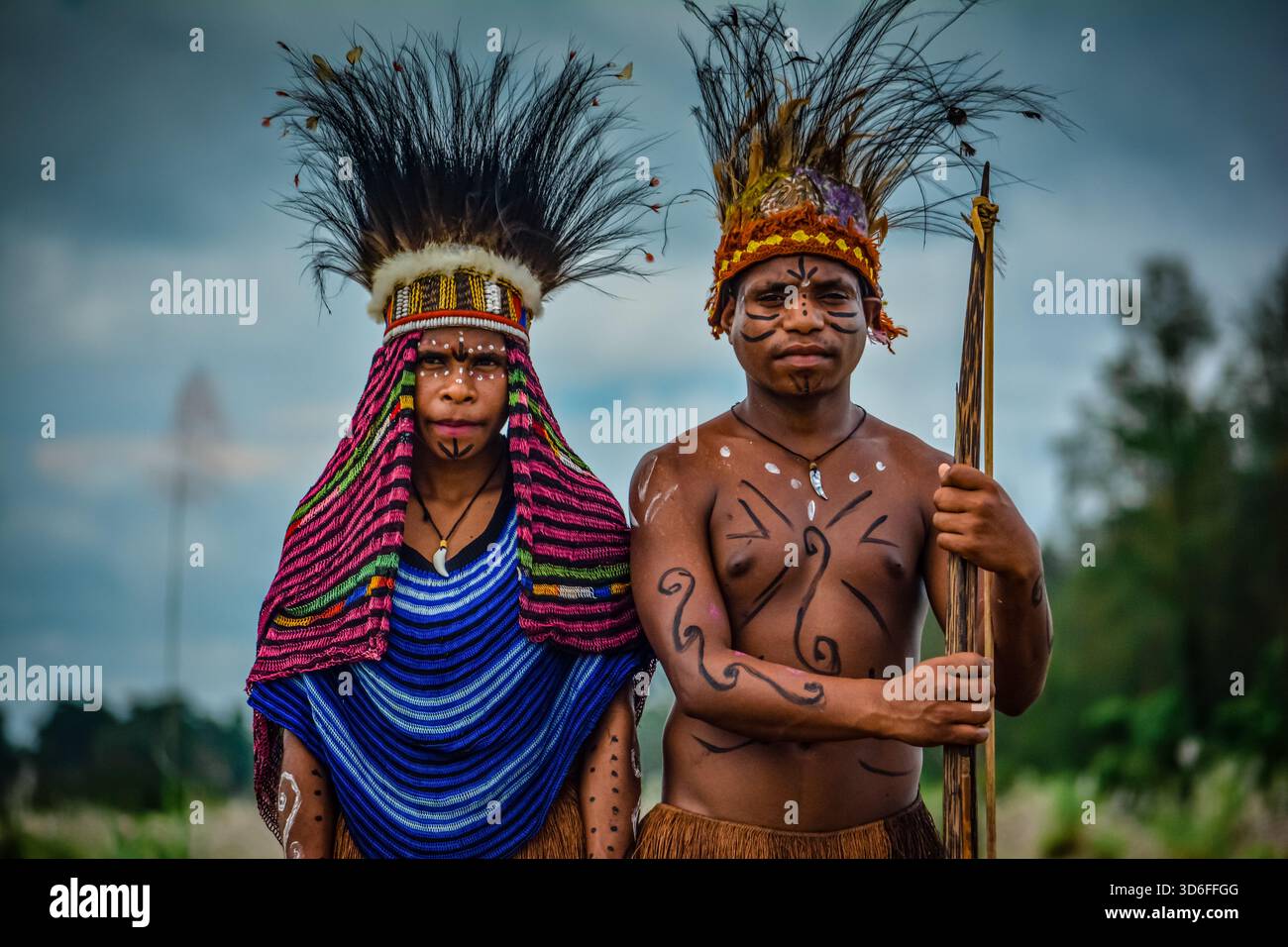 Gli uomini e le donne indigene papuesi si stagliano all'aperto indossando abiti tradizionali, copricapi e vernice per il corpo, riflettendo il ricco patrimonio culturale. Foto Stock