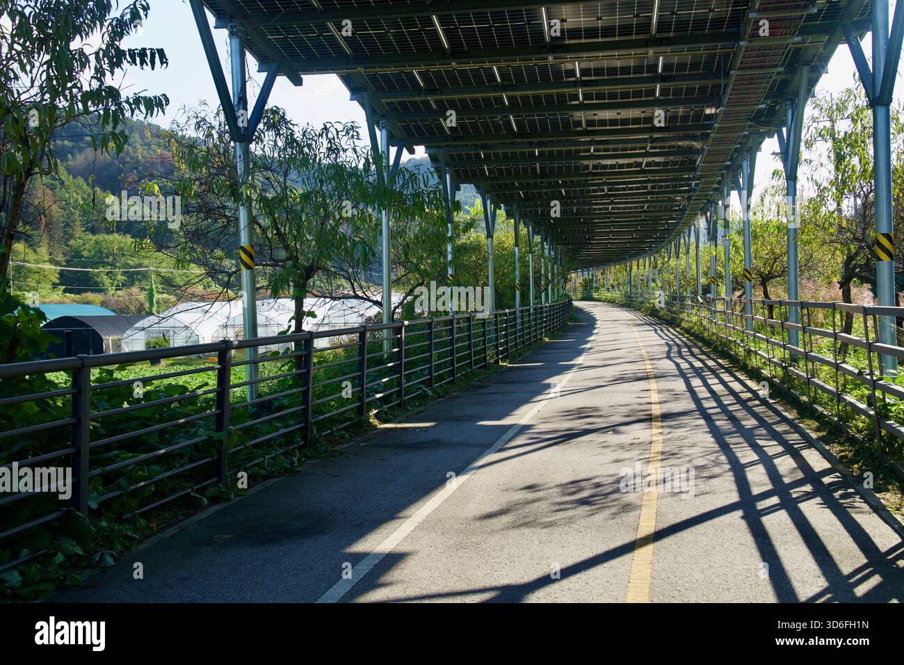 Un tratto curvo del sentiero ciclabile di Bukhangang corre sotto pannelli solari accanto a frutteti e serre vicino al torrente Daljeon a Gapyeong, con pomeriggio Foto Stock