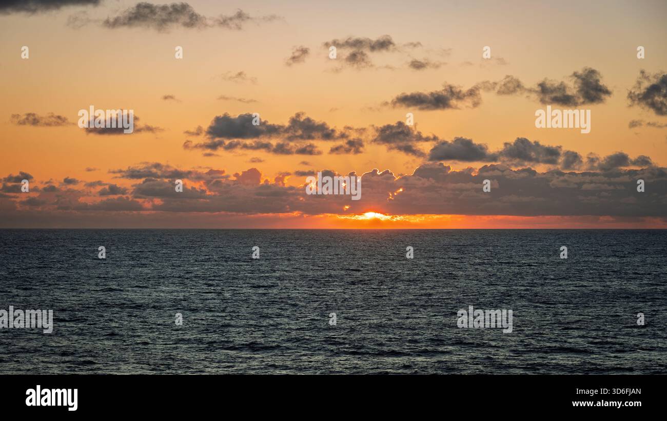 Il sole tramonta all'orizzonte, proiettando un caldo bagliore sull'acqua e sulle nuvole Foto Stock
