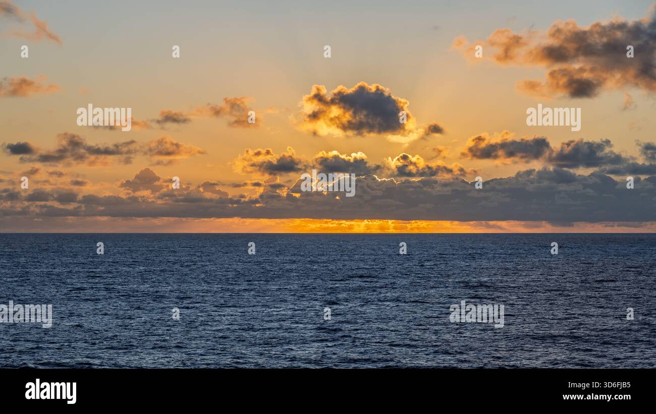 Il sole tramonta all'orizzonte, proiettando un caldo bagliore sull'acqua e sulle nuvole Foto Stock