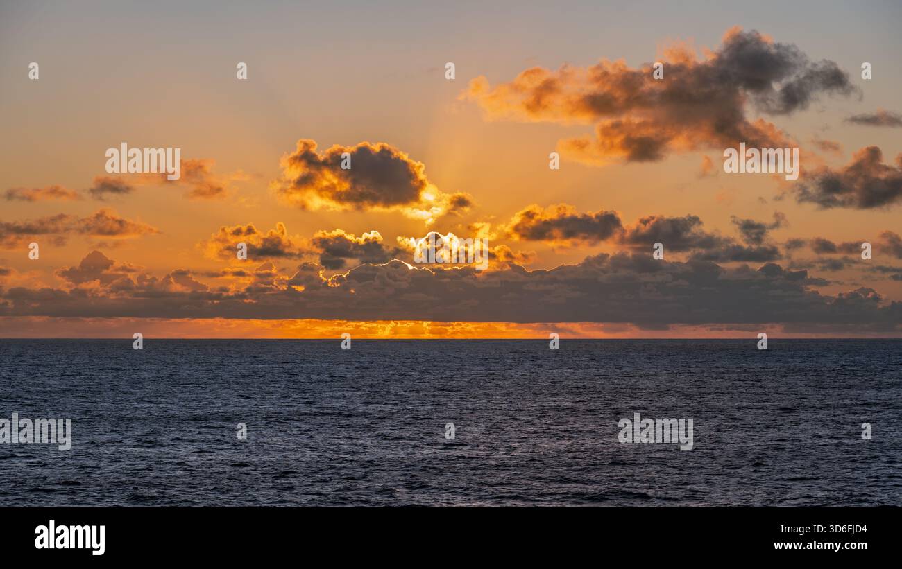 Una foto del sole che tramonta all'orizzonte, proiettando un caldo bagliore sull'acqua e sulle nuvole Foto Stock