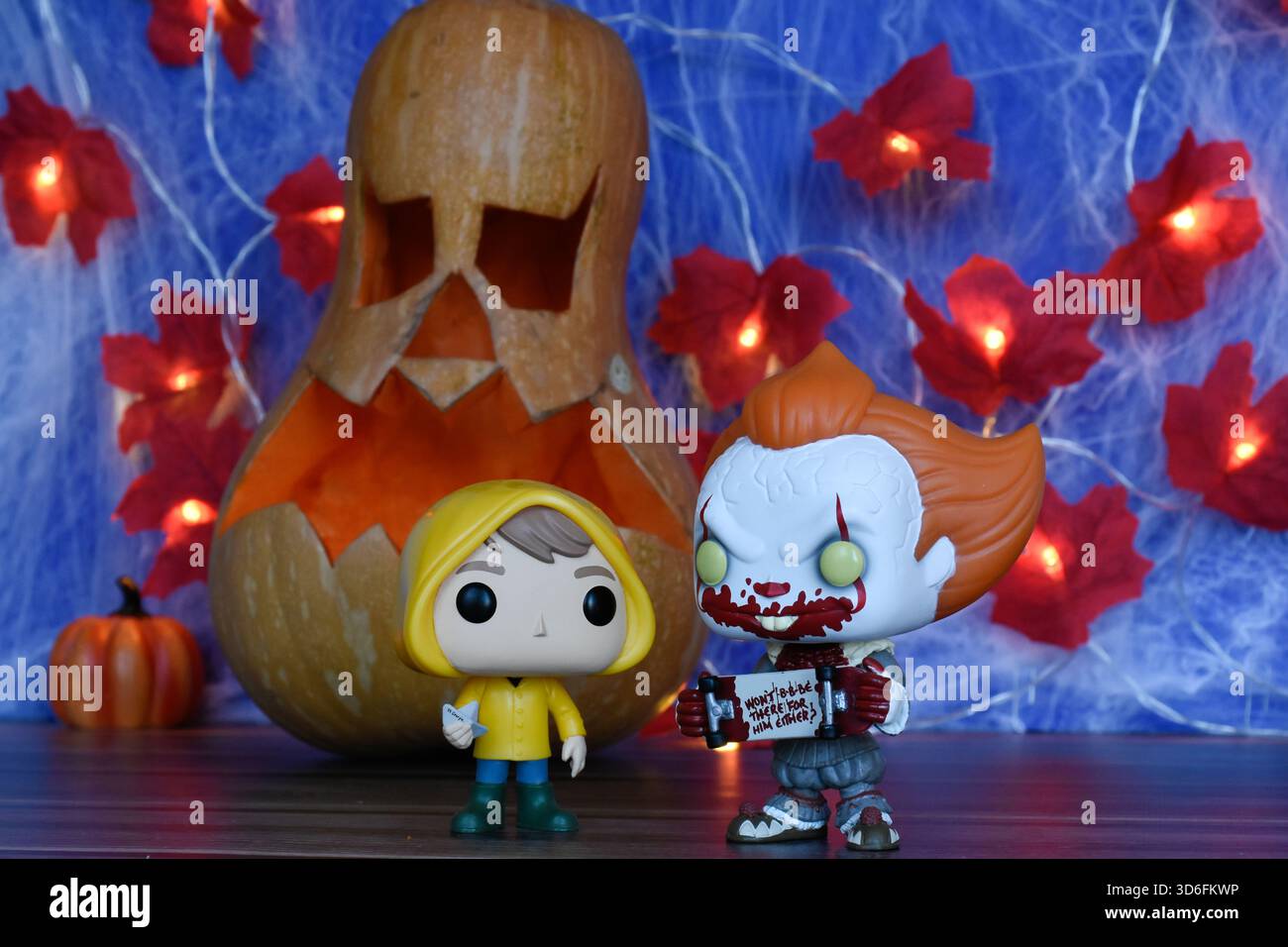 Funko Pop action figure di clown Pennywise e Georgie del film horror IT. Arredamento di Halloween, Jack o lanterna, ragnatela, foglie, luci. Foto Stock