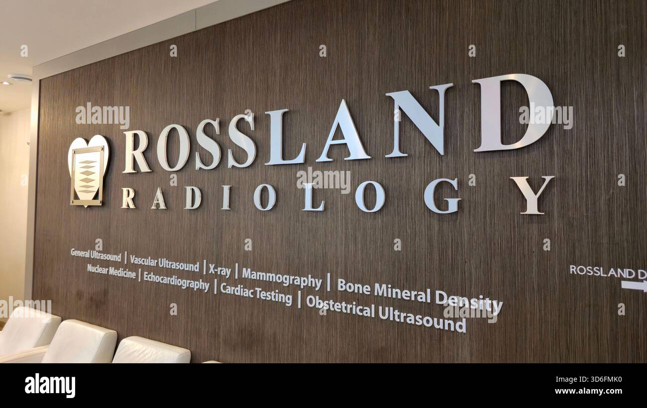 Cartello da parete Rossland Radiology con scritta e logo metallici, che elenca i servizi diagnostici accanto alle sedie d'attesa bianche. - Immagine stock catturata con smartphone