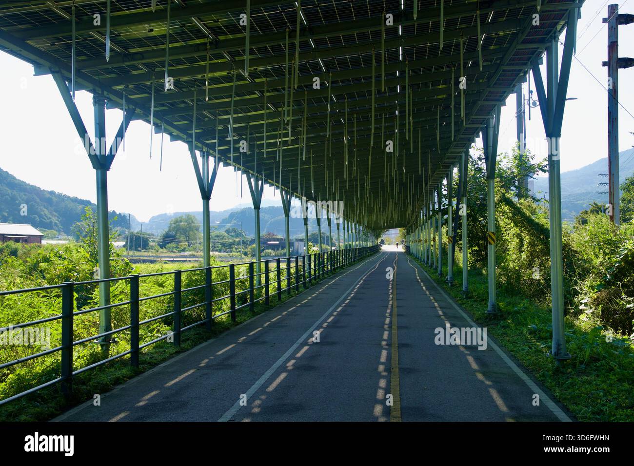 Guardando sotto un tetto fotovoltaico, il sentiero ciclabile di Bukhangang attraversa le fattorie lungo il fiume Daljeon a Gapyeong, con rotaie e fissaggi sospesi Foto Stock