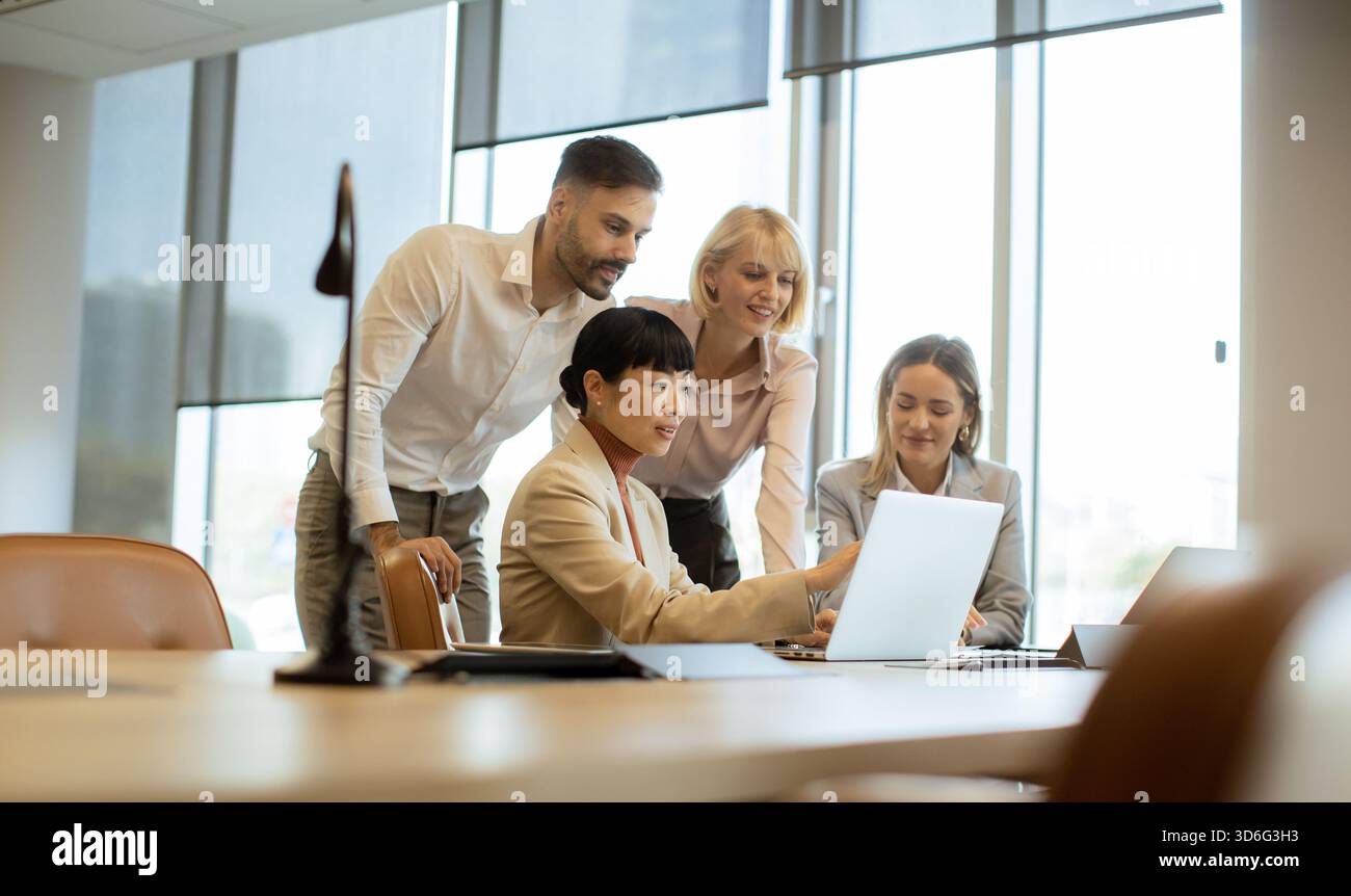 Quattro professionisti si riuniscono intorno a un notebook in un ufficio luminoso. Discutono di idee e condividono informazioni, lavorando insieme per risolvere problemi e innovare. Foto Stock