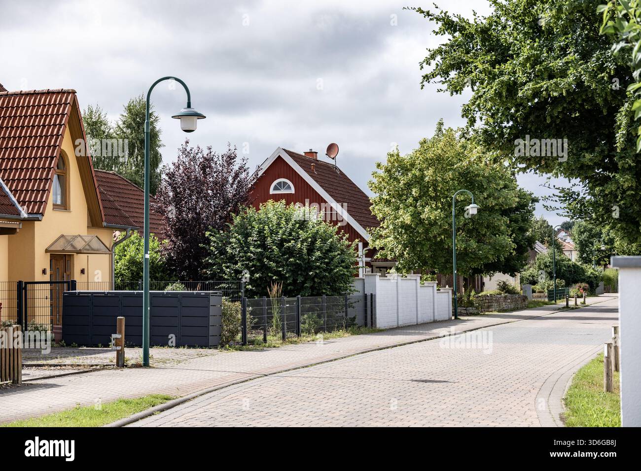 Tranquilla strada residenziale con case colorate, alberi e lampioni tradizionali in un quartiere periferico in una nuvolosa giornata estiva Foto Stock