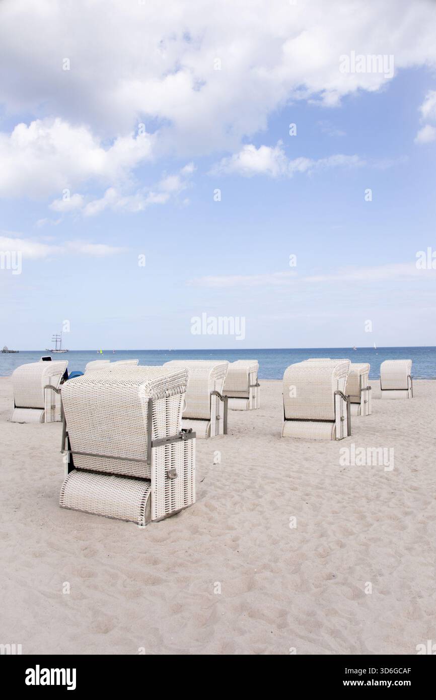 Spiaggia vuota con sedie a sdraio in vimini bianco di fronte al mare sotto il cielo blu con nuvole Foto Stock